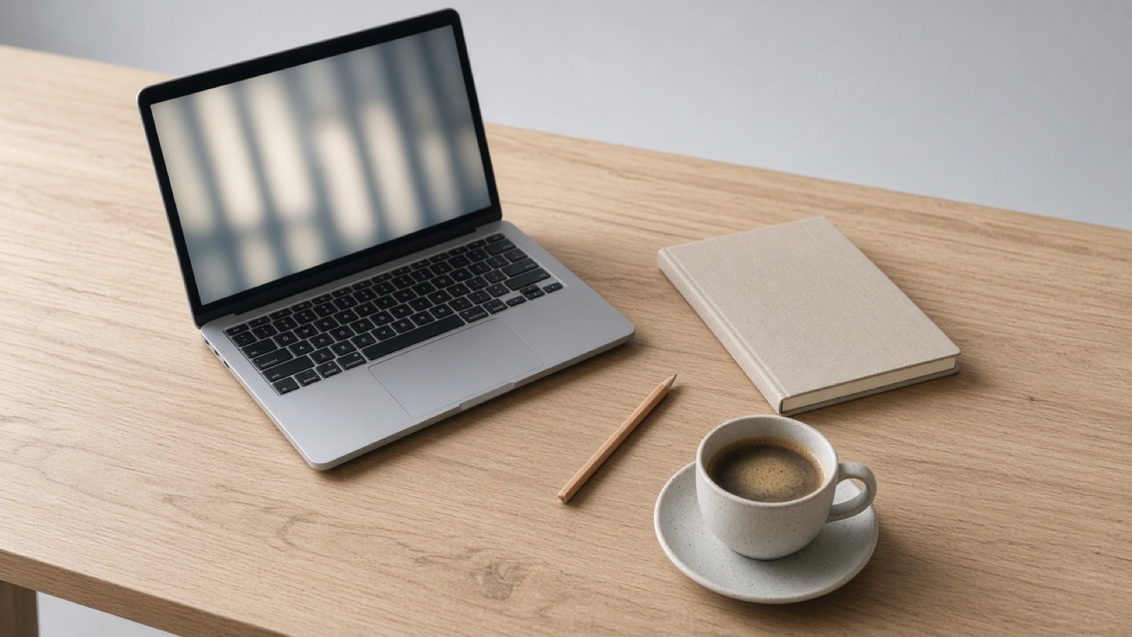 A laptop, a closed notebook, and a cup of coffee on a desk